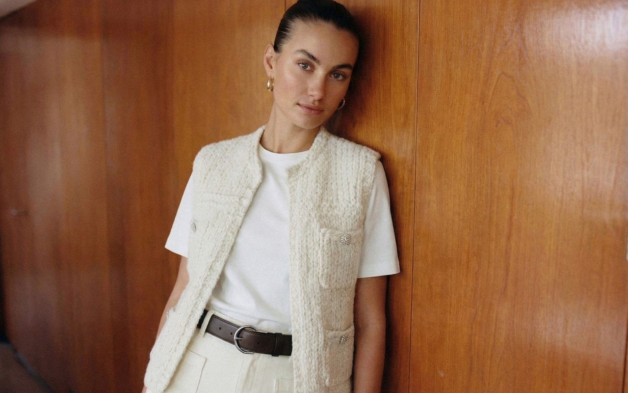 Frau mit weißem T-Shirt und weißer Strickweste mit weißer Hose.