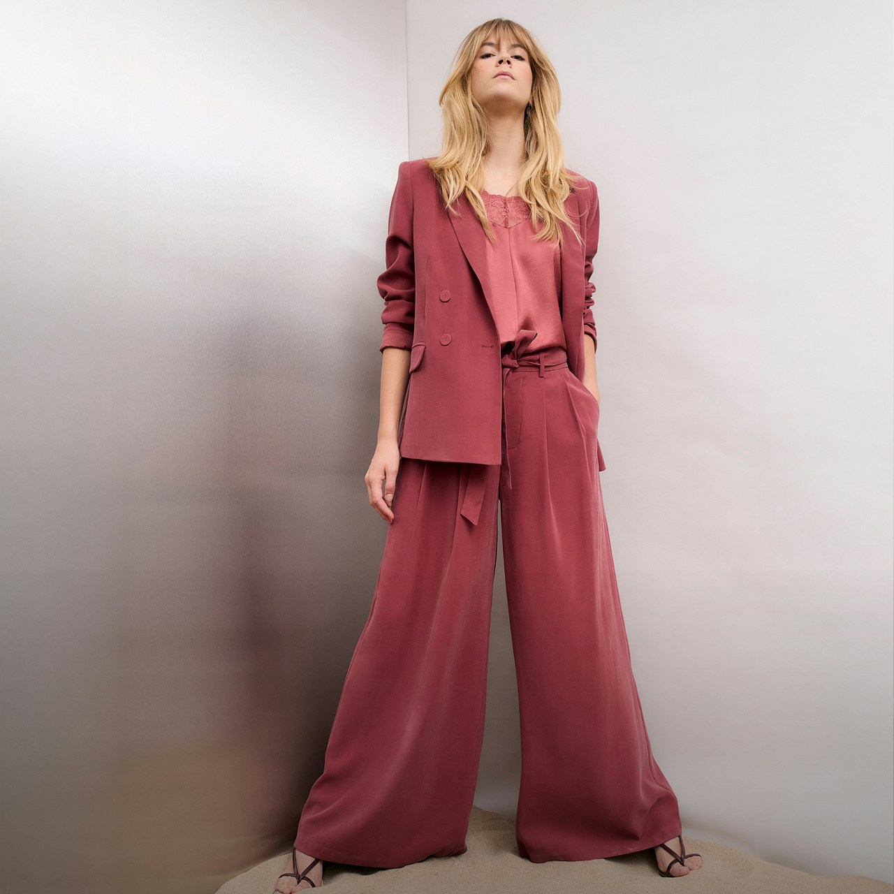 Woman in a raspberry-coloured suit consisting of a blazer and wide-leg trousers with a pink blouse top.