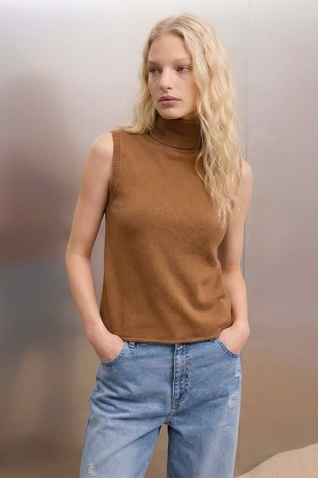 Frau mit braunem Rollkragen Pullover ohne Ärmel und Jeanshose.