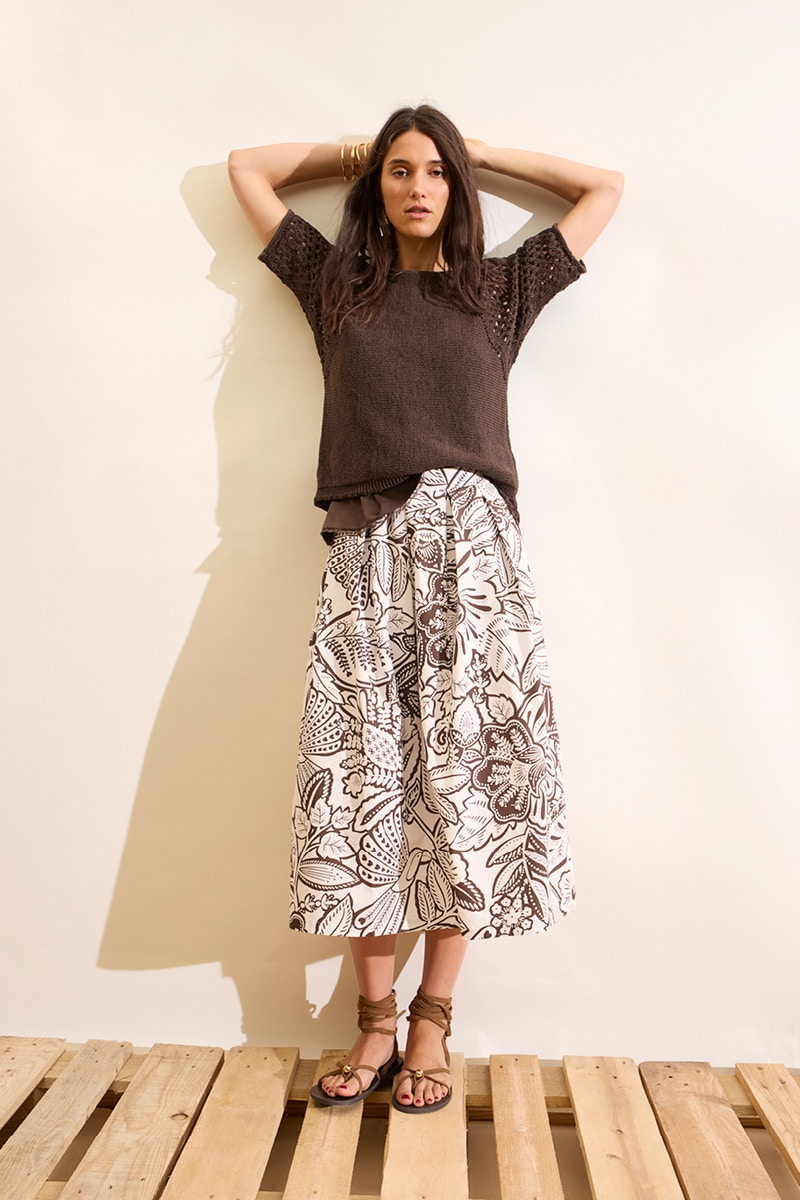 Frau mit braunem Pullover und weißem Midi-Rock mit braunem Blumenmuster.