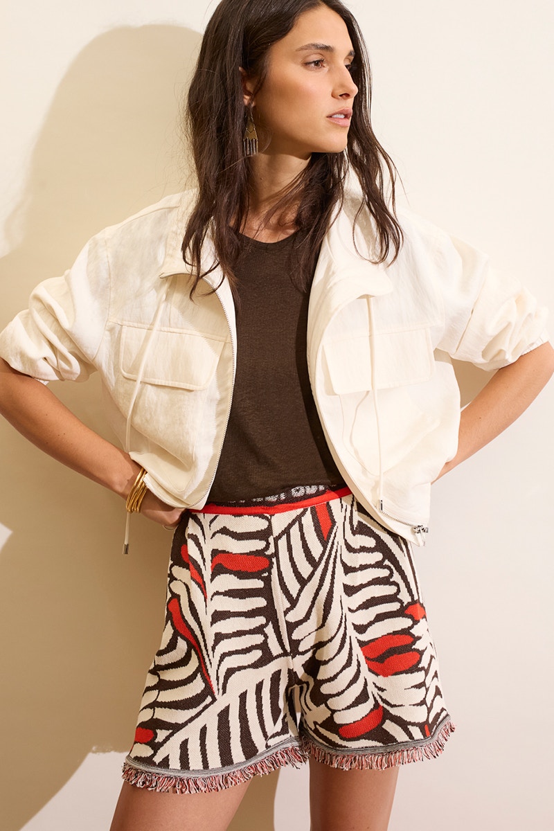 Woman wearing a white jacket, brown shirt and shorts in white, red and brown leaf pattern.