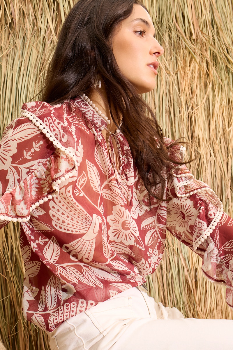 The woman is wearing a red and white blouse with a floral print and white trousers.