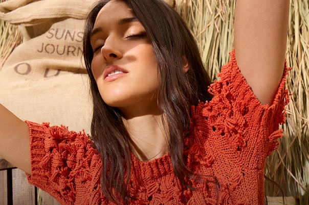 The woman is wearing an orange jumper with fringes.