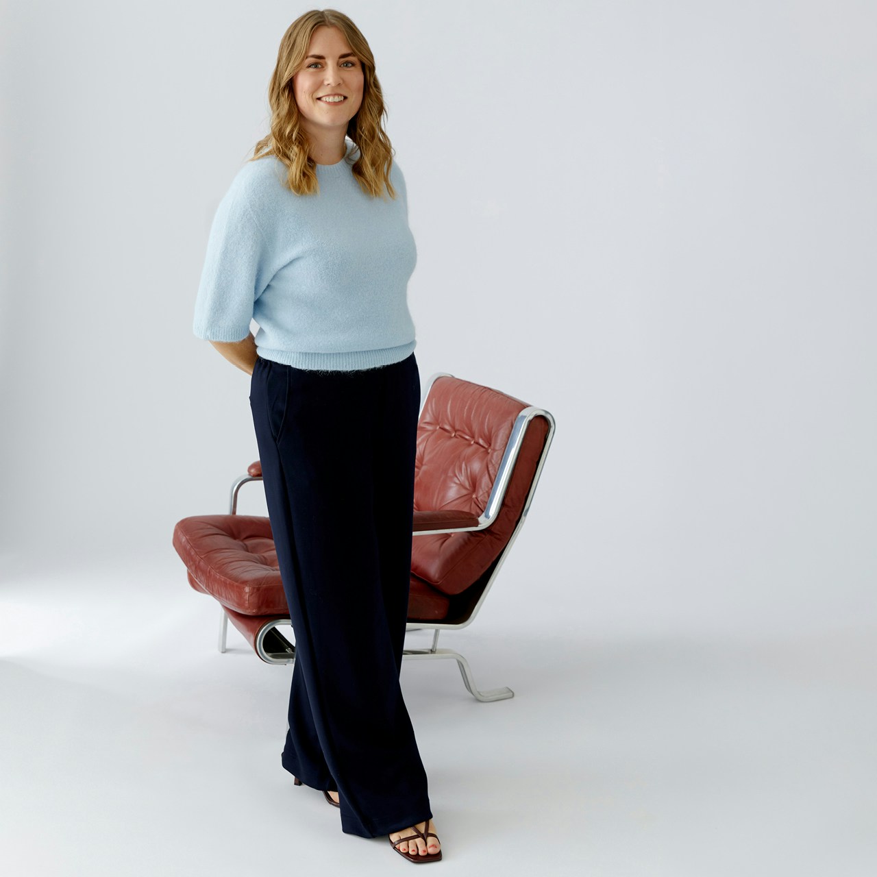 Eva is wearing a light blue knitted jumper with dark blue straight-leg trousers.