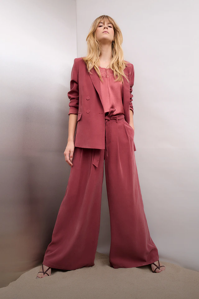 Frau trägt einen berry-farbenen Anzug aus Blazer und weiter Hose und ein pinkes Top.