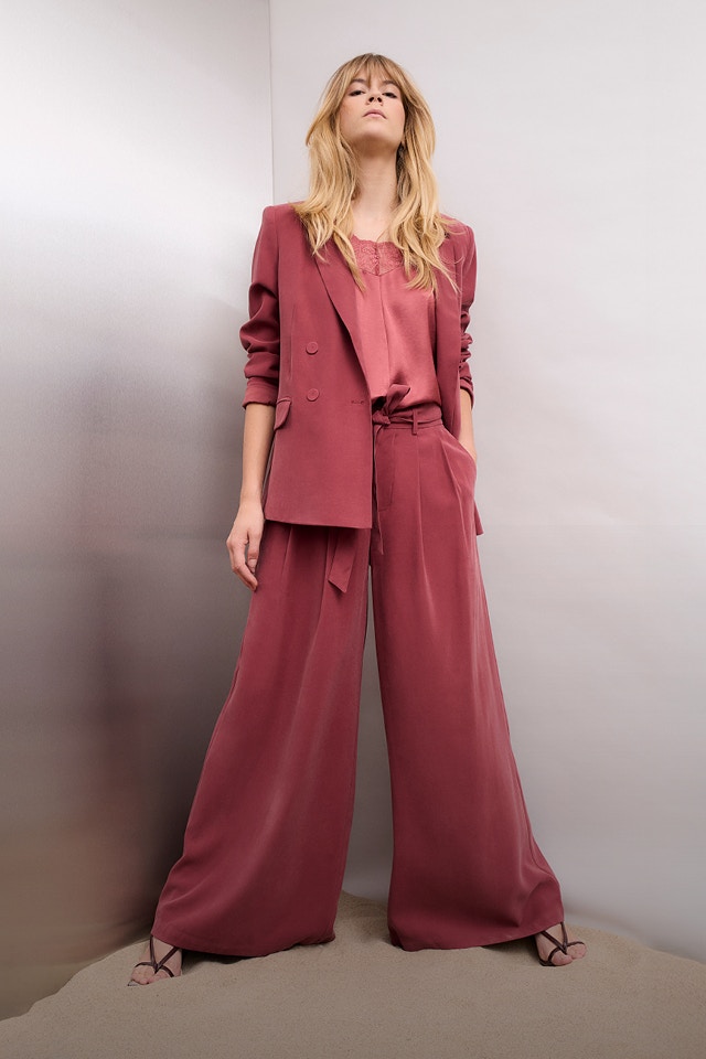 Woman wearing a berry-coloured suit consisting of a blazer and wide-leg trousers, and a pink top.