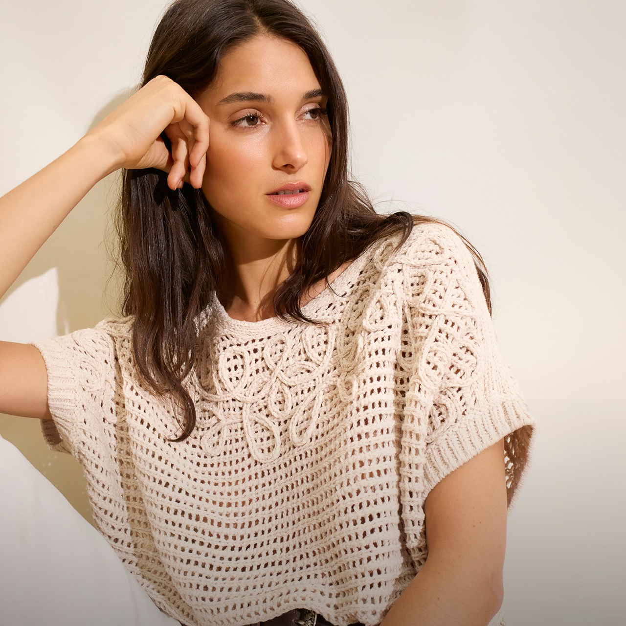 Woman wearing a beige crochet-style jumper and white trousers