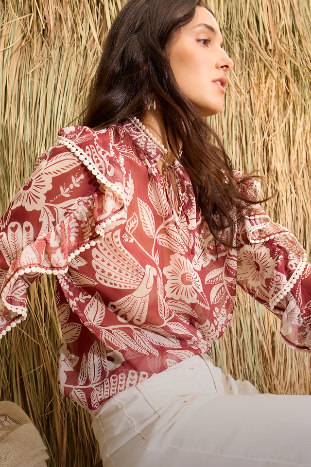 The woman is wearing a red and white blouse with a floral print and white trousers.