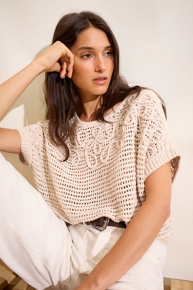 Model wears a knitted jumper with drawstring detailing, paired with beige and white jeans