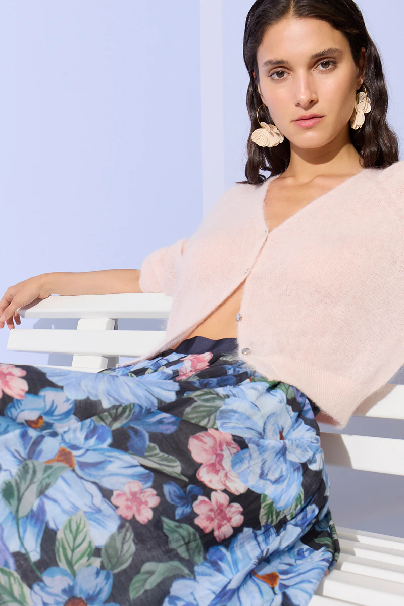 Frau mit einer pastelrosa Strickjacke und einem geblümten Rock in hellblau, dunkelblau, rosa und grün.