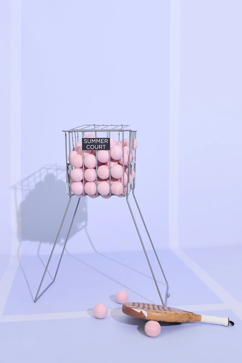 A basket containing pink tennis balls and a leather paddle.