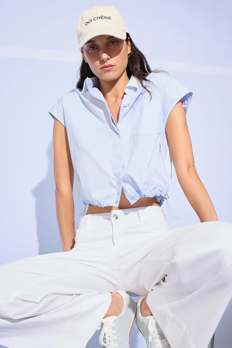 A woman wearing a light blue blouse and white trousers.