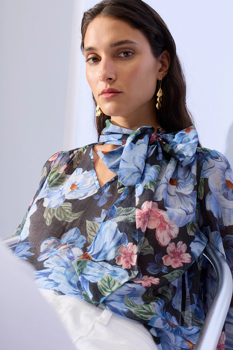 A woman wearing a floral blouse in light blue, dark blue, pink and green, paired with white trousers.