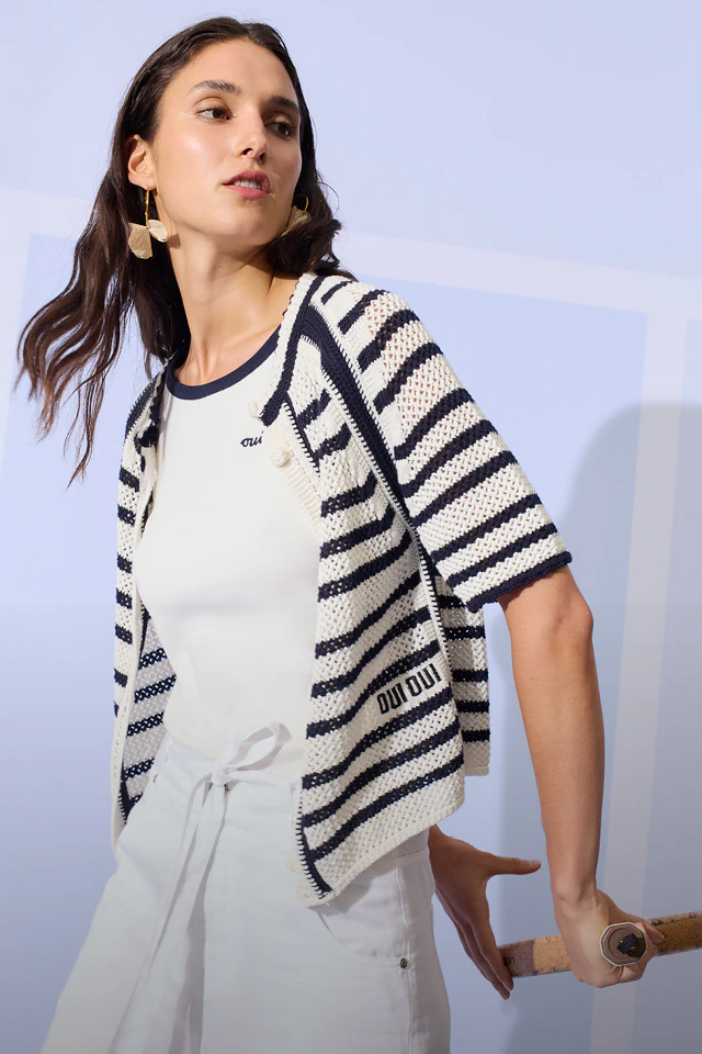 Frau mit weißem T-Shirt und blau-weiss gestreifter Strickjacke und weißer Hose.