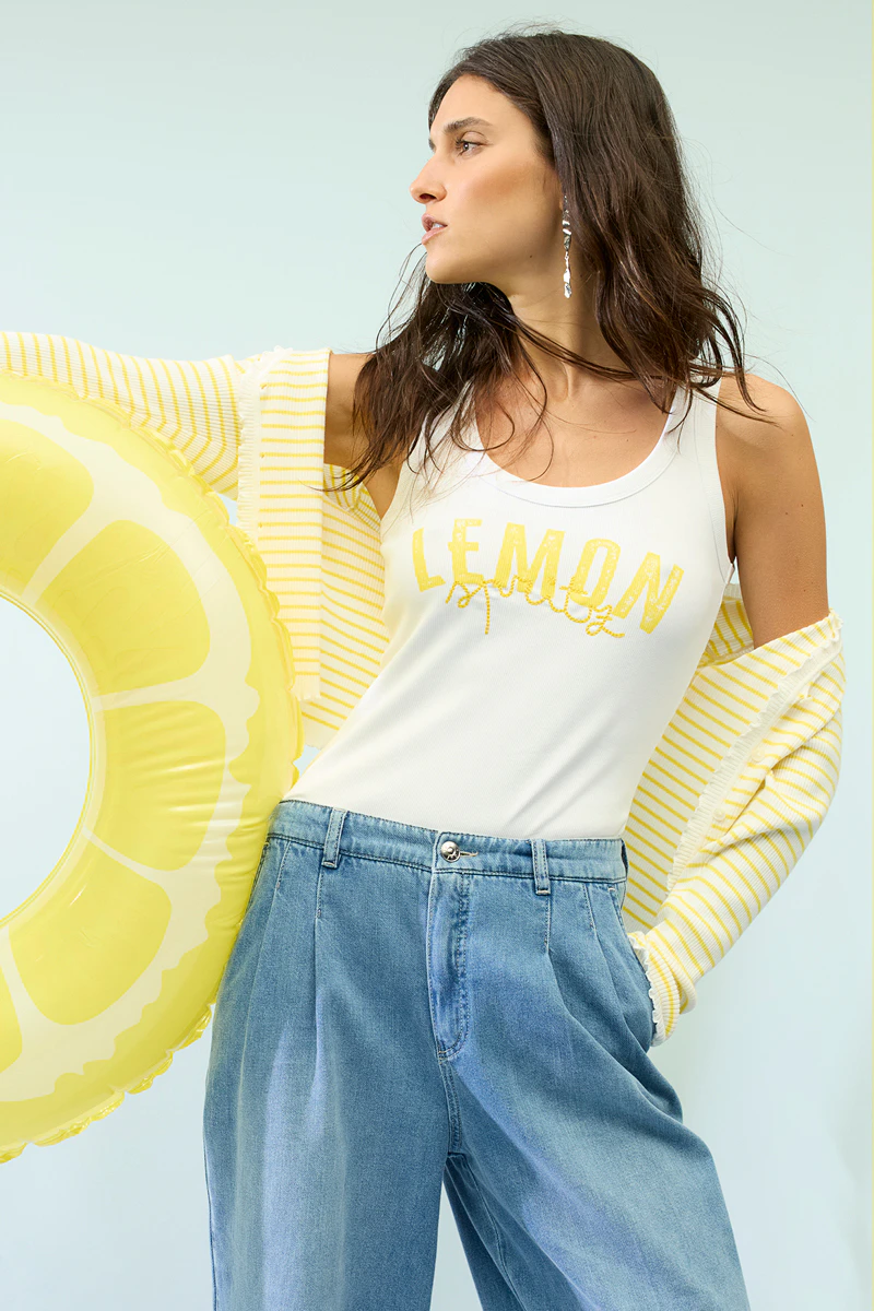 Frau trägt eine gelb-weiss gestreifte Strickjacke, ein weißes Top mit gelber Schrift Lemon und einer Jeans.