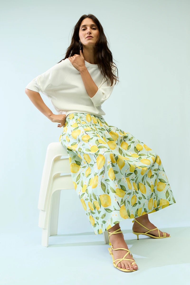 The woman is wearing a white jumper and a loose-fitting skirt with a lemon print.