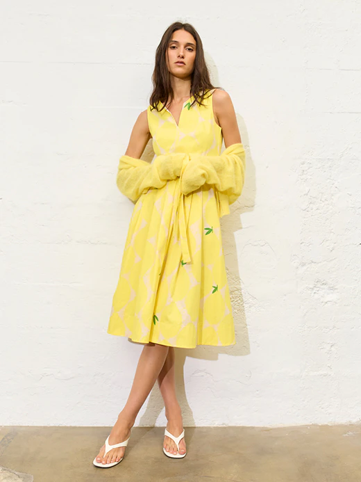 A woman wearing a yellow dress with a lemon print and a matching yellow cardigan.