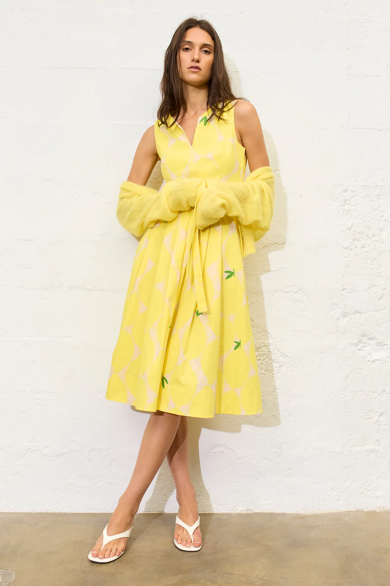 A woman wearing a yellow dress with a lemon print and a matching yellow cardigan.