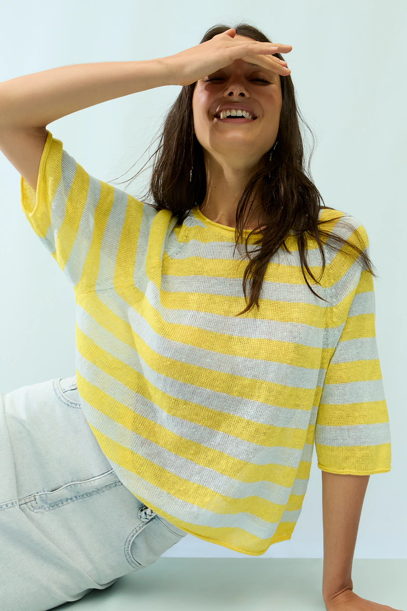 A woman is wearing a yellow and white striped jumper with a white skirt.