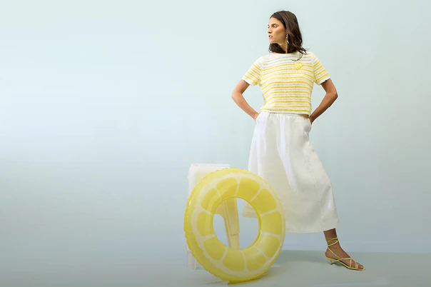 The woman is wearing a yellow and white striped short-sleeved jumper and a white skirt.