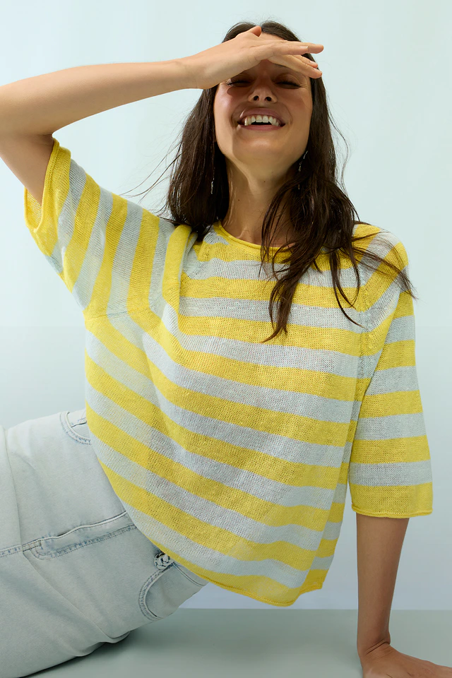 A woman is wearing a yellow and white striped jumper with a white skirt.