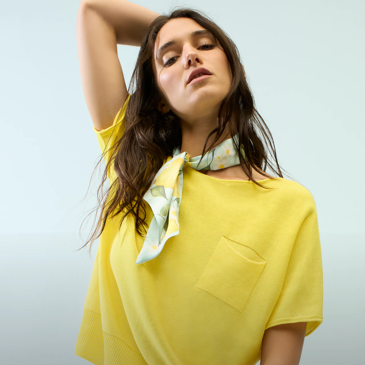 A woman wearing a yellow jumper, a scarf with a lemon print and white trousers.