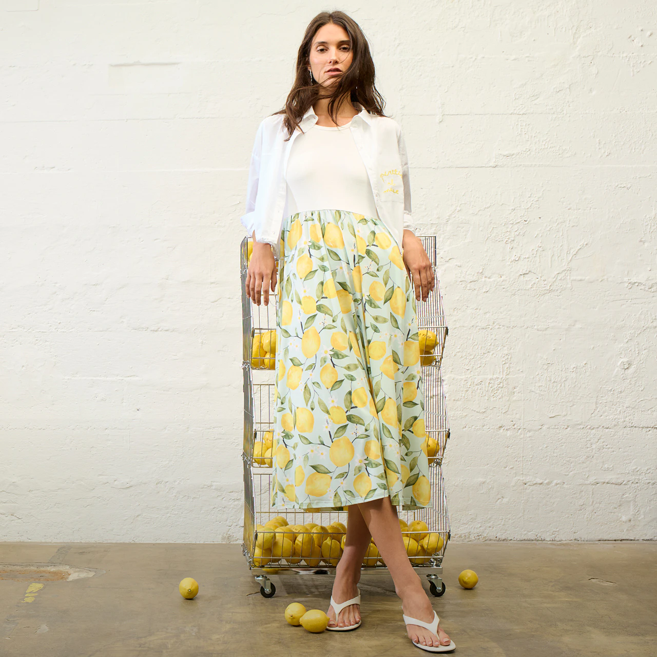 A woman wearing a dress with a white top and a lemon-print skirt, paired with a white jacket.