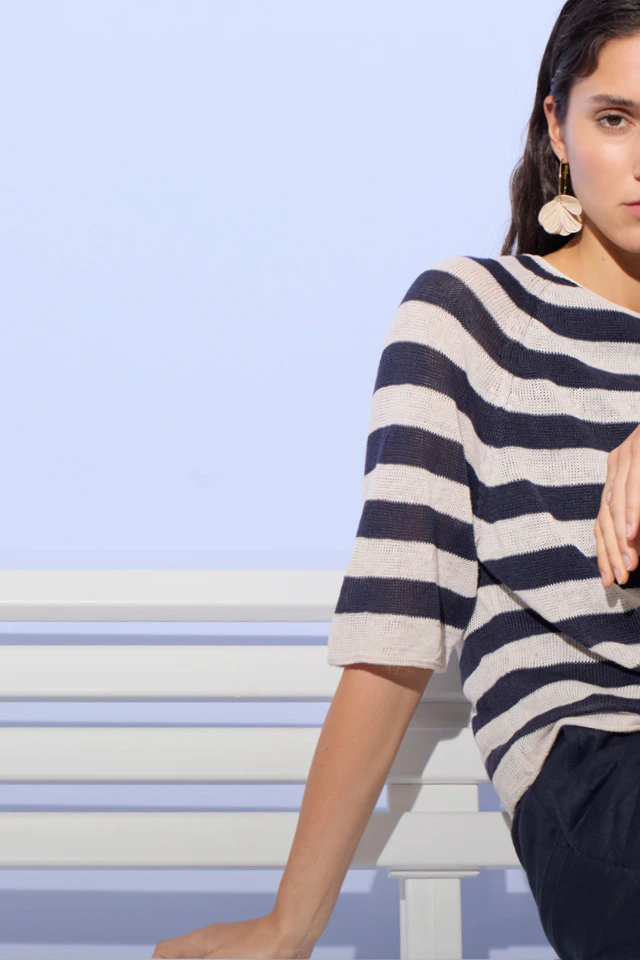 A woman wearing a white and blue striped jumper and dark blue trousers.