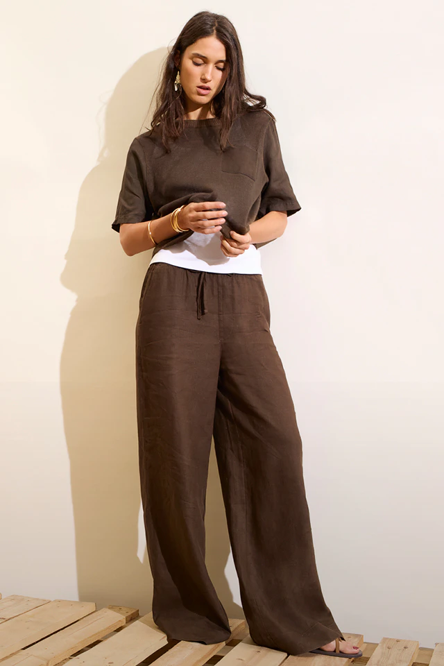 A woman is wearing a brown blouse with a white T-shirt underneath and matching brown trousers.