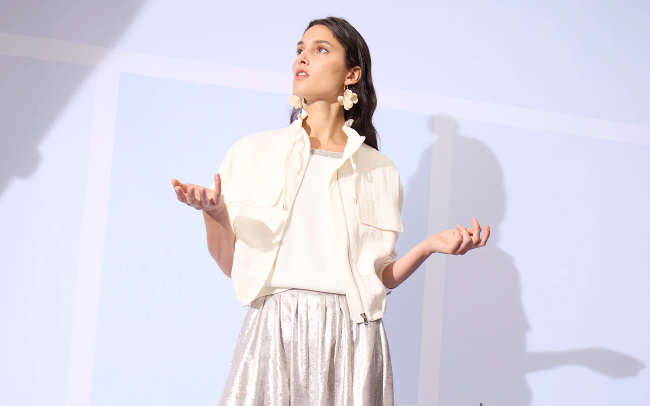 Frau mit weisser Jacke, weissem Shirt und silberfarbenen Rock.