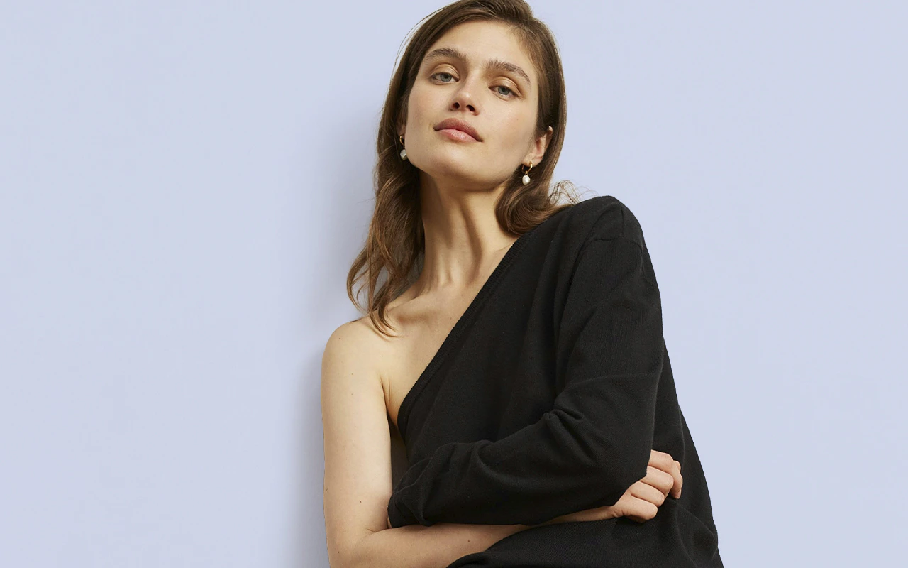 The woman is wearing a black top with an asymmetrical collar, leaving one shoulder bare.