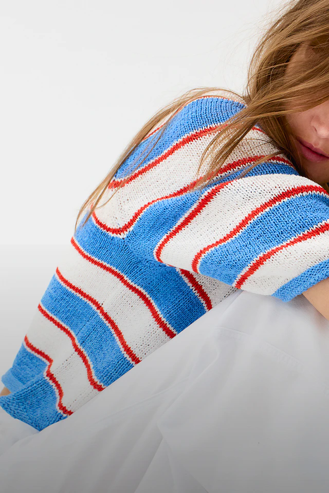 Frau mit einem kurzarm Pullover in weiss-blau und roten Blockstreifen und weisser Jeans.