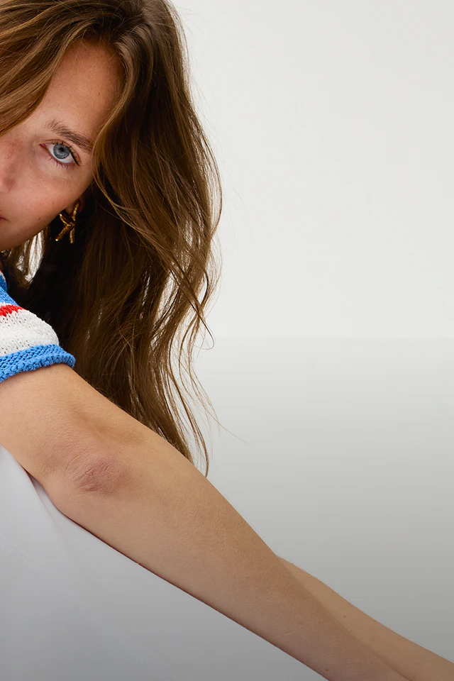 A woman wearing a short-sleeved jumper with white, blue and red block stripes and white jeans.