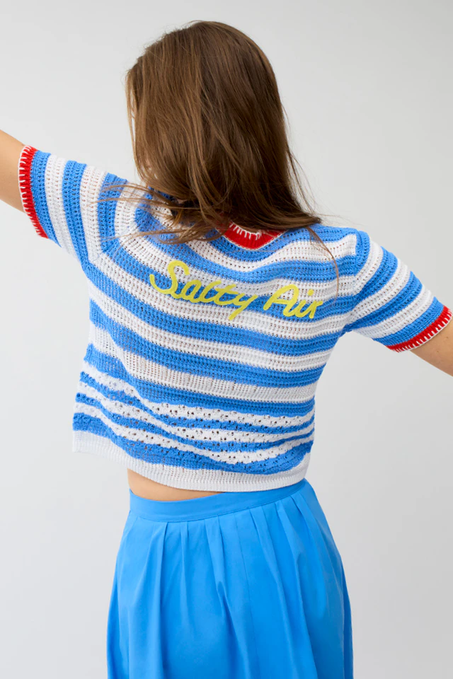 A woman seen from behind, wearing a blue and white striped jumper with red trim and yellow embroidery on the upper back; she is also wearing a blue skirt.