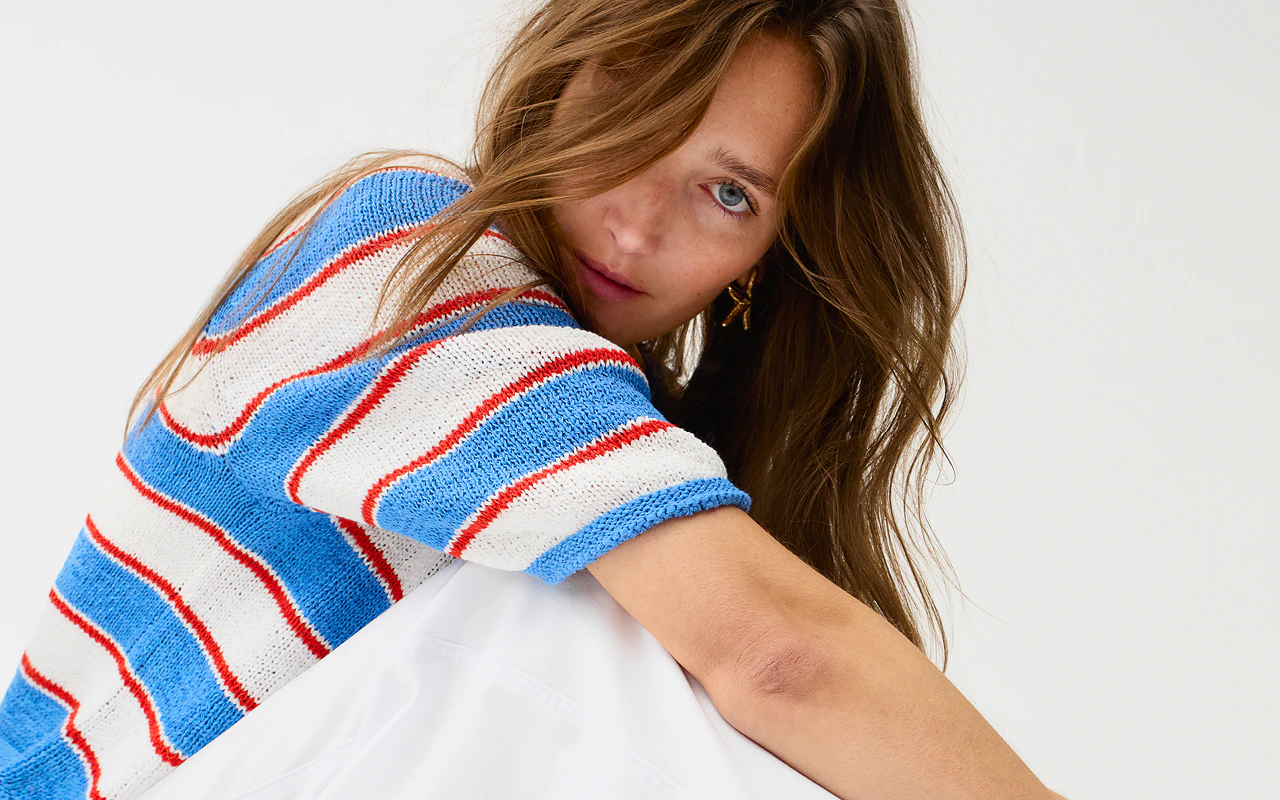 A woman wearing a short-sleeved jumper with white, blue and red block stripes and white jeans.