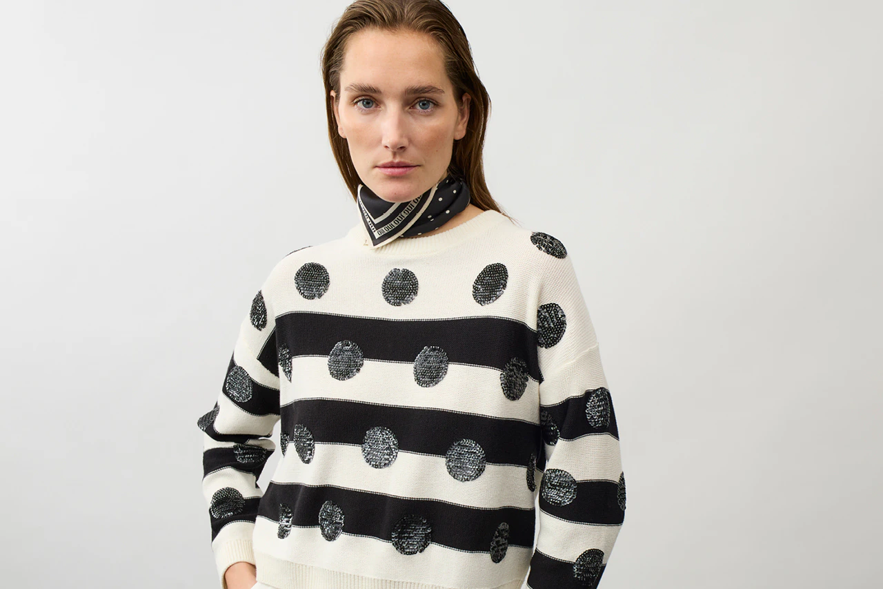 Frau mit einem schwarz weiss gestreiften Pullover mit schwarzen Pailetten Punkten und einem Halstuch in schwarz-weiss.