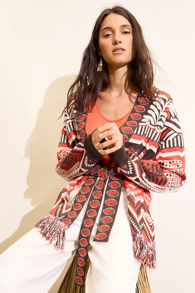 Model wears a red and orange patterned knitted cardigan with fringed details