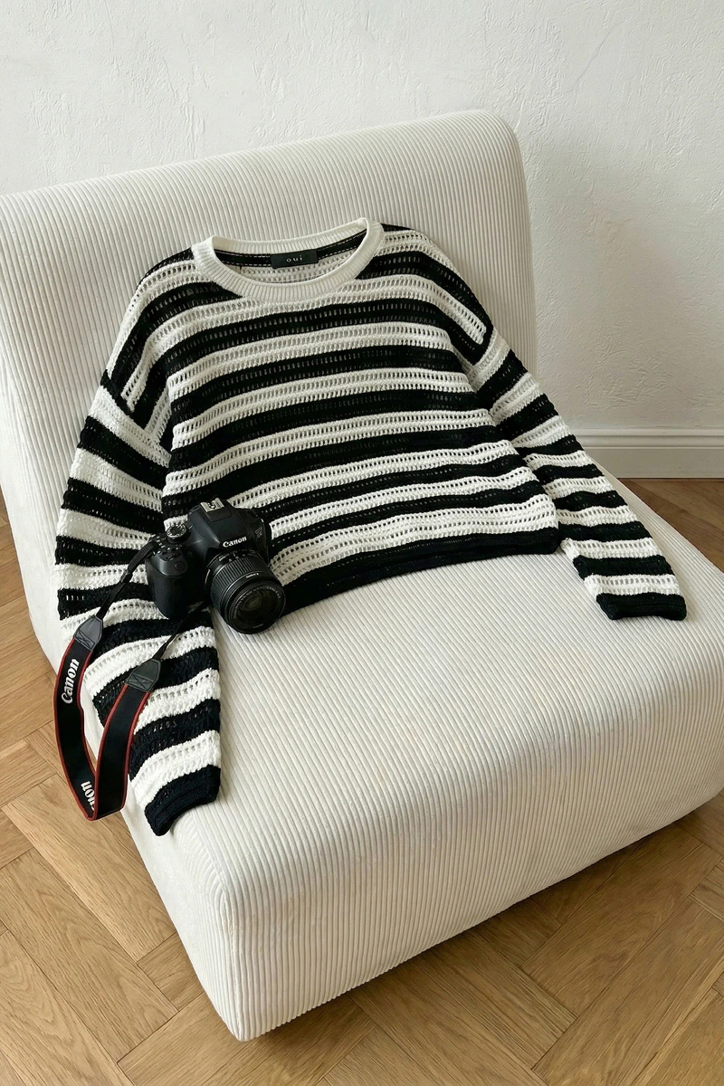 Auf einem weissen Sessel liegt ein Pullover in schwarz weiss gestreift.