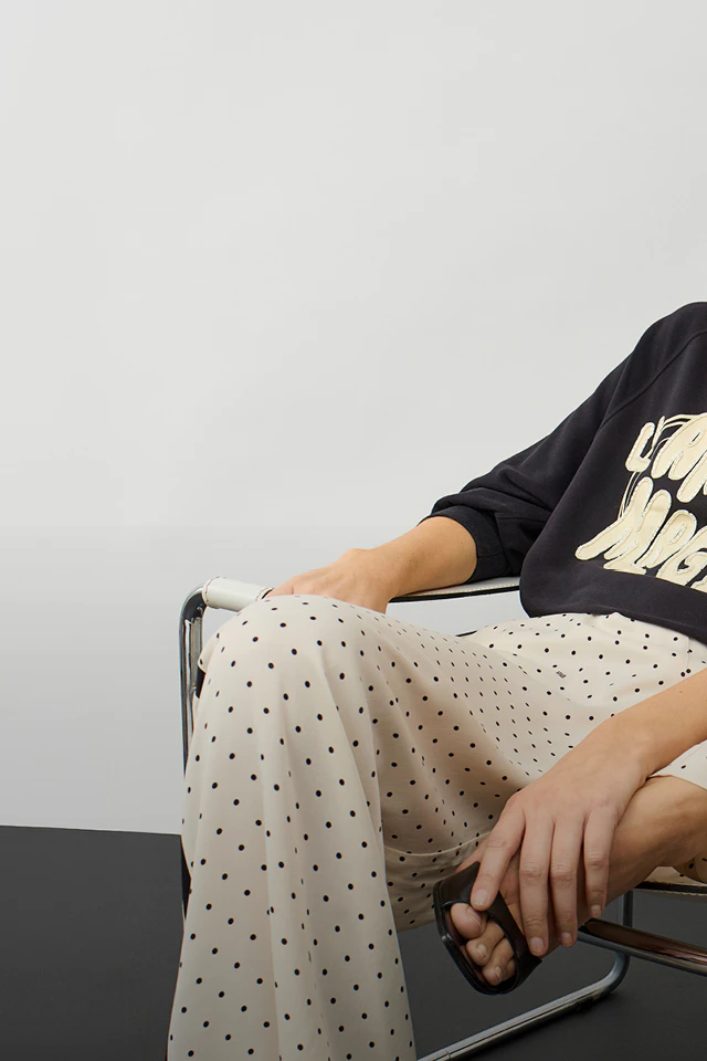 A woman wearing a black jumper with white lettering and white trousers with black dots.