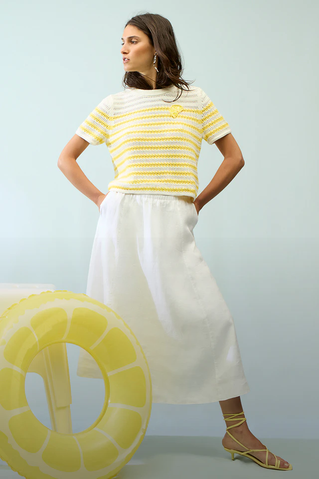 A woman wearing a yellow and white striped jumper and a white skirt.