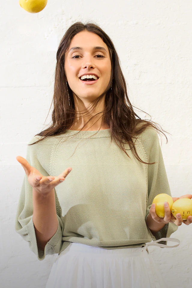 Frau mit gruenem Pullover und weißem Rock.