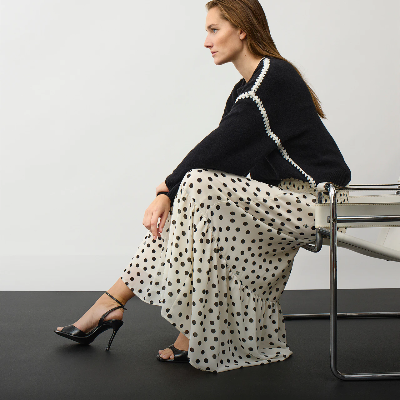 The model is wearing a black-and-white polka-dot maxi dress with a black jumper