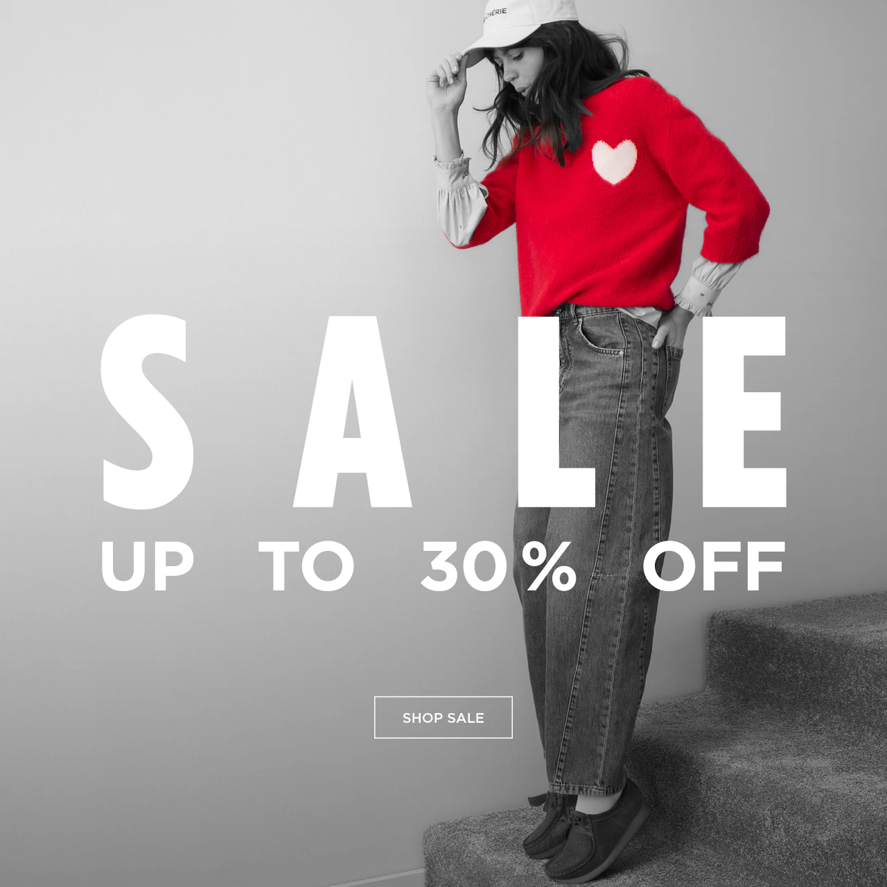 Bild in schwarz/weiss/grau gehalten, zeigt eine Frau mit einem roten Pullover mit weißem Herz und Schrift: SALE up to 30% OFF mit Klickfläche shop sale