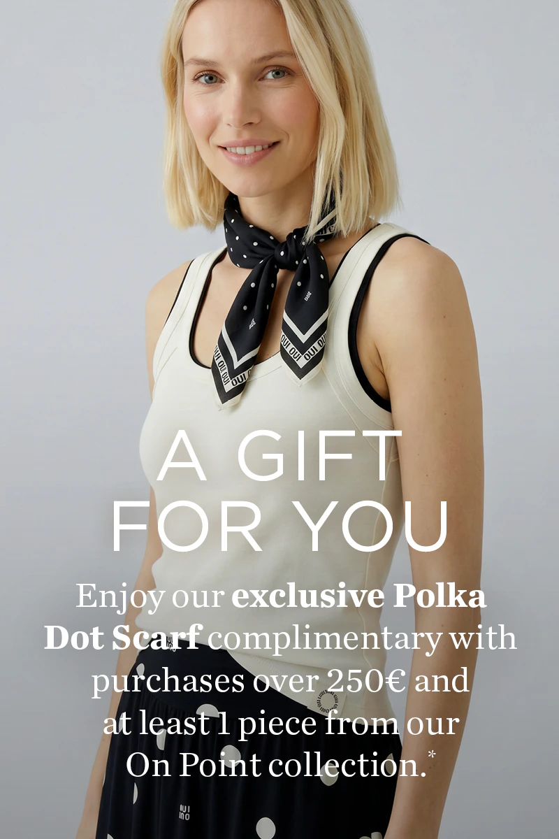 Woman wearing a white top and a black-and-white scarf. A gift for you: enjoy our exclusive polka dot scarf compimentary with purchases over 250€ and at least  1 piece from our On Point collection.