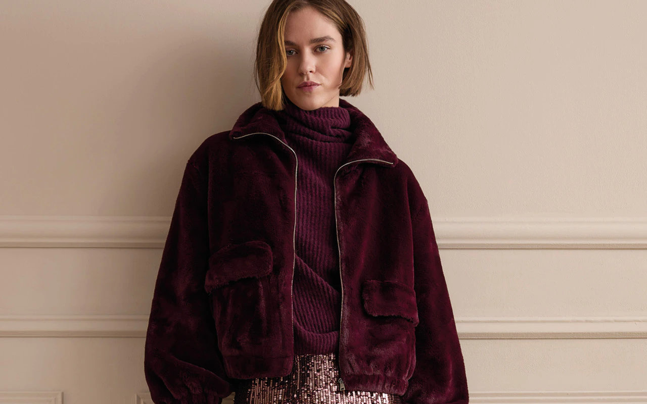 Model trägt kuschelige Jacke und Strickpullover in bordeauxrot darunter.