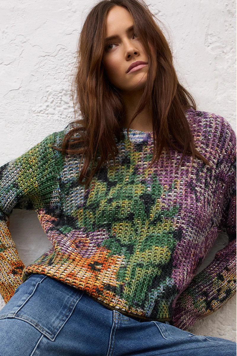 Frau mit gestricktem Pullover in großen Blumenmuster, dazu Jeans.