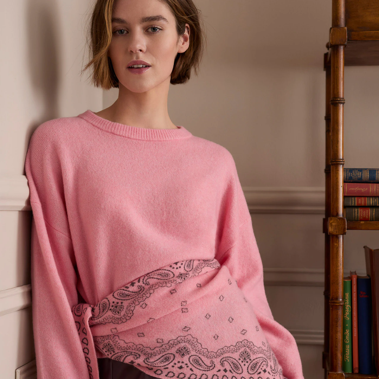 The model is wearing a pink jumper and a pink knitted triangular scarf with a bandana pattern.