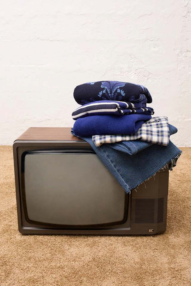 A pile of Oui garments in blue, including a jumper, a checked blouse and jeans, are lying on a vintage television.