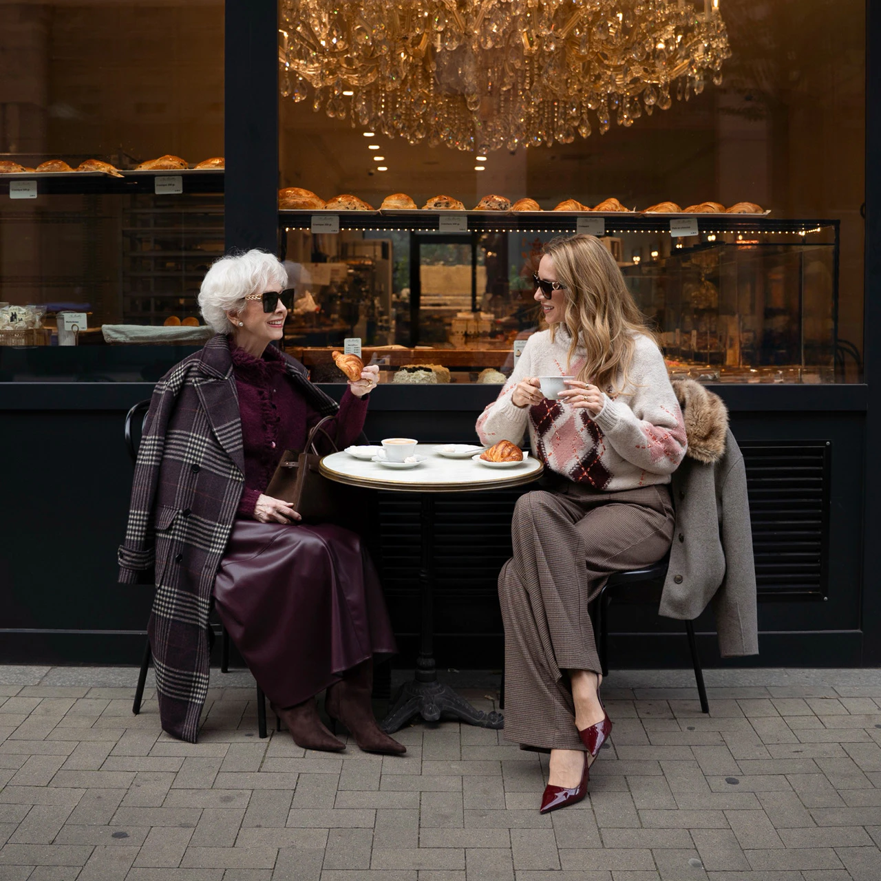 Influencerin Alexandra Lapp und ihre Mutter sitzen bei Kaffee und Gebäck vor einem Café und tragen Oui Mode.