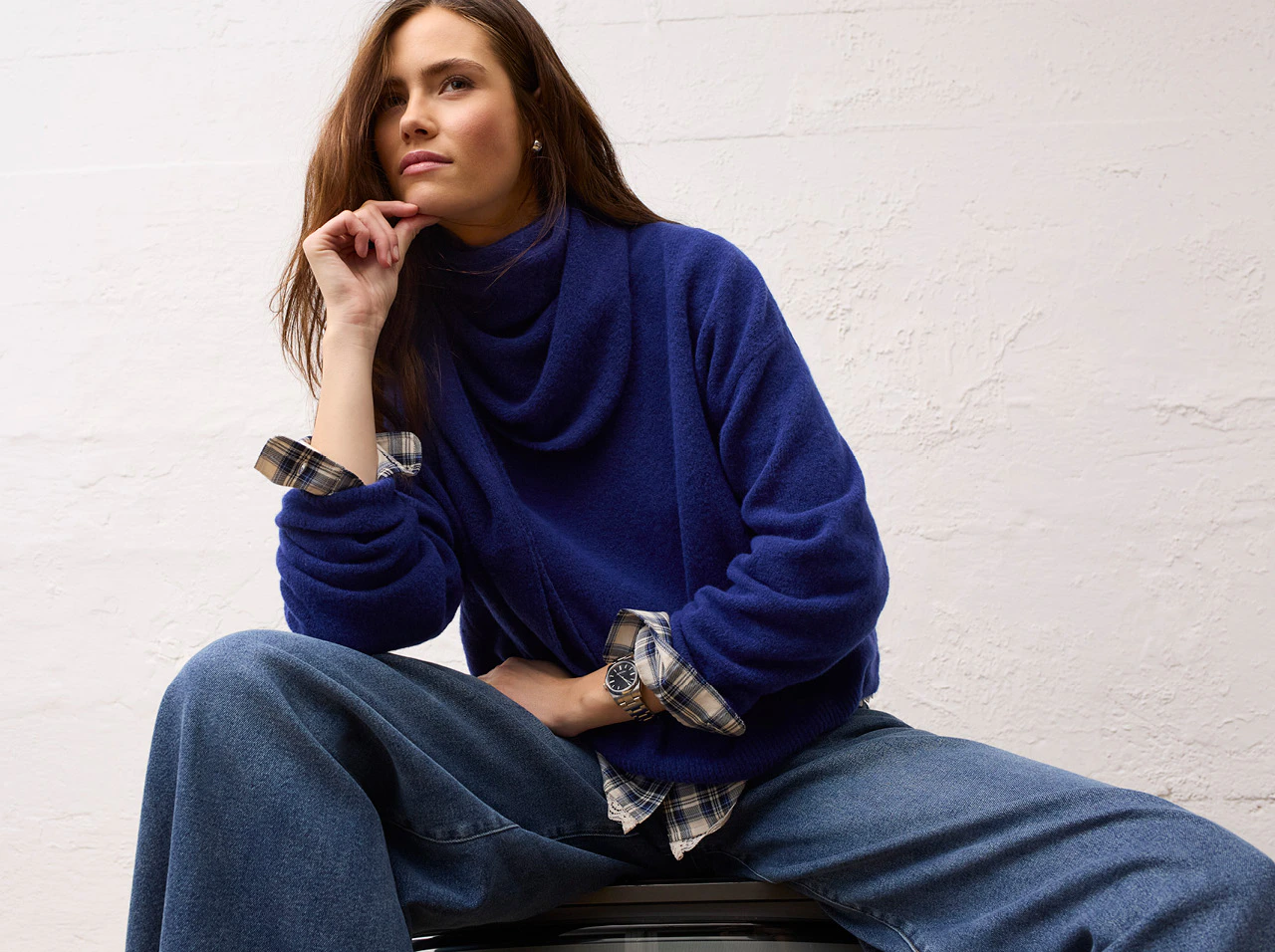 Model trägt einen blauen Pullover mit weitem Kragen, darunter eine karierte Bluse und eine weite Jeans aus der OUI Heritage Reset Kollektion.